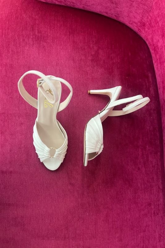 Sandalias Inés blancas con tira al tobillo sobre un sillón fucsia