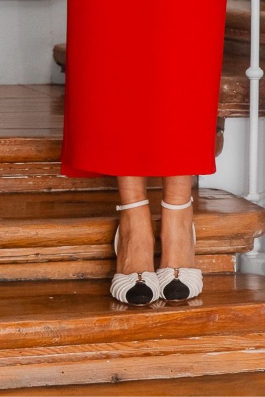 Zapatos Inés R blancos con puntera negra y vestido rojo en una escalera
