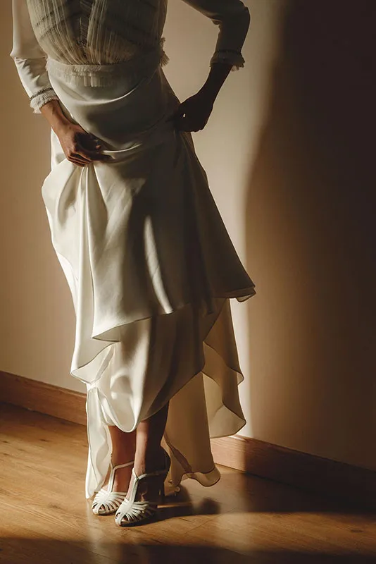 Novia recogiéndose el vestido con sandalias Brenda en color crema