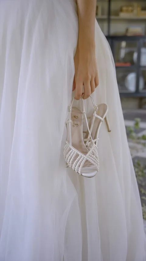 Novia sujetando sandalias Sidney de tiras blancas