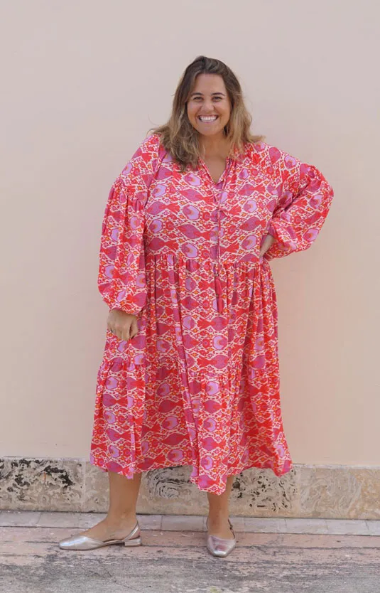 Mujer sonriente con vestido rosa estampado y bailarinas Ana plateadas